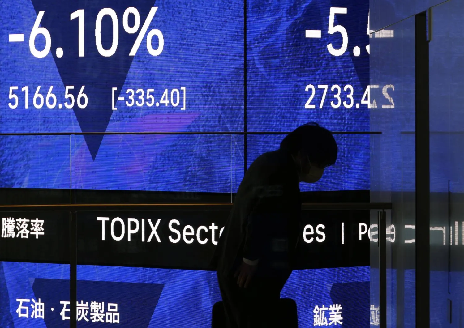 رجل يقف أمام لوحة مؤشرات سوق الأسهم في طوكيو